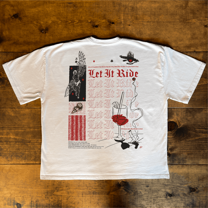 Let It Ride oversized tee in bone laid flat on a wood table, showing the full back print