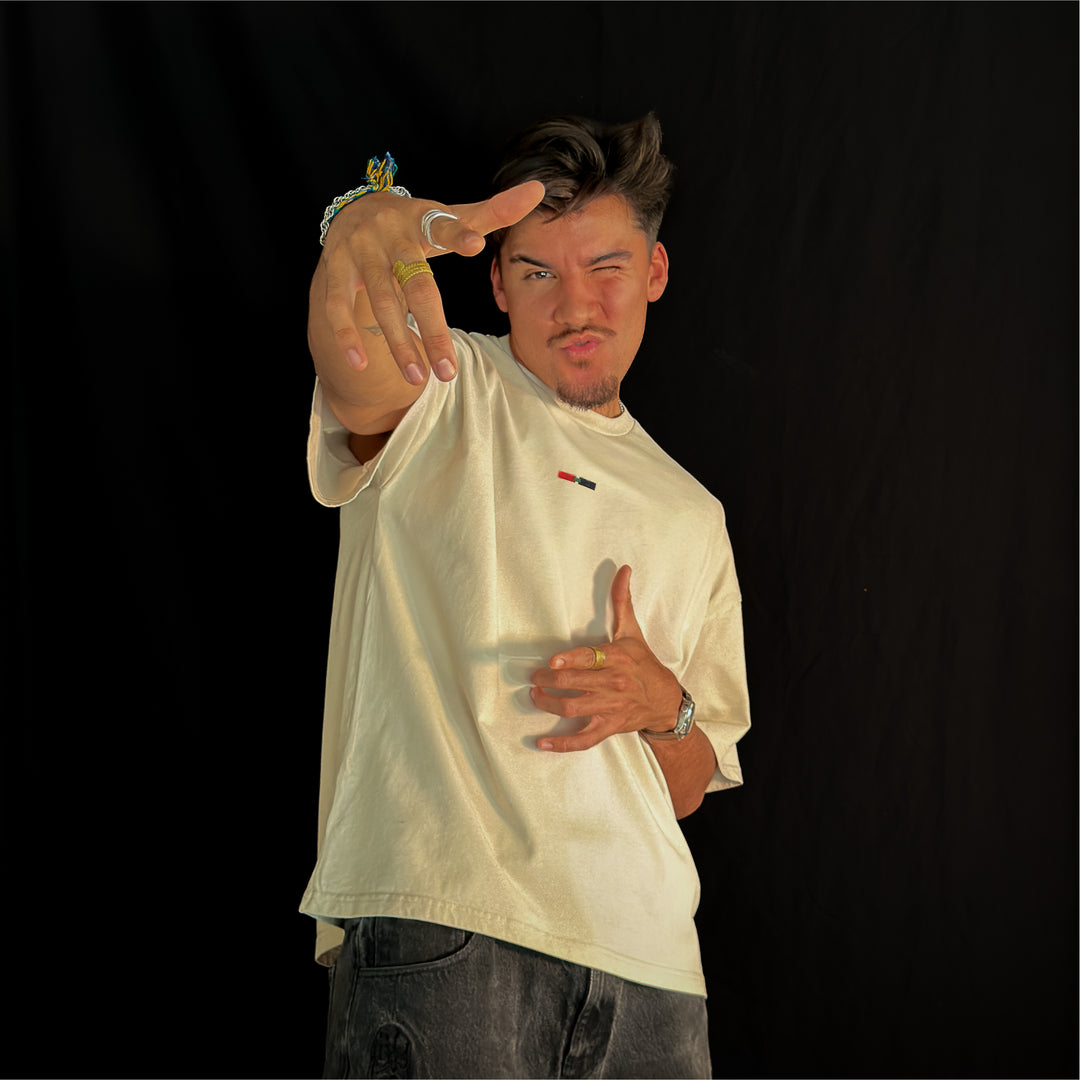 Man wearing the Let It Ride oversized tee in bone, seen from the front, pointing at the camera, with the small red, green and black stripe on the chest